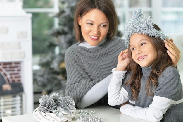 Retrato de joven madre y su hija con adornos navideños sentados en la mesa