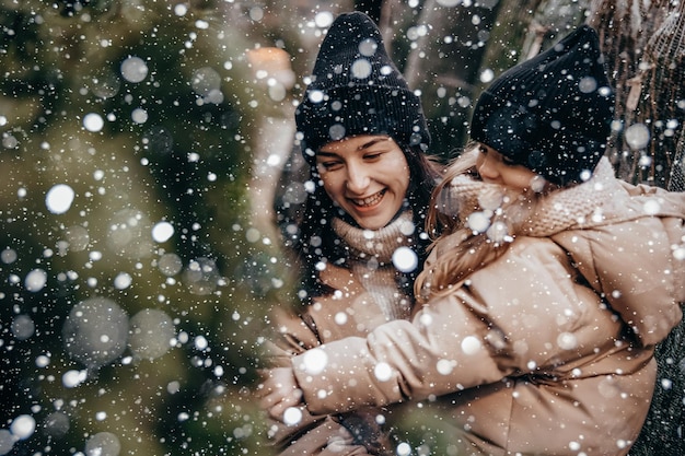 Retrato de una joven madre con su hija en brazos, sonríen y se regocijan en la nevada Elegir y comprar un árbol de Navidad en el mercado navideño