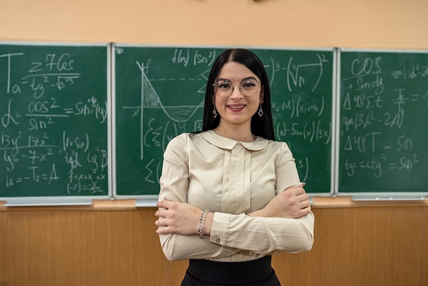 Retrato de una joven maestra contra la pizarra con fórmula matemática en el aula