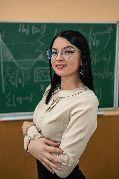 Retrato de una joven maestra contra la pizarra con fórmula matemática en el aula