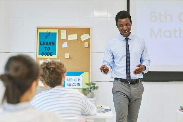 Retrato de un joven maestro negro sonriendo alegremente en clase mientras presenta el tema a los niños
