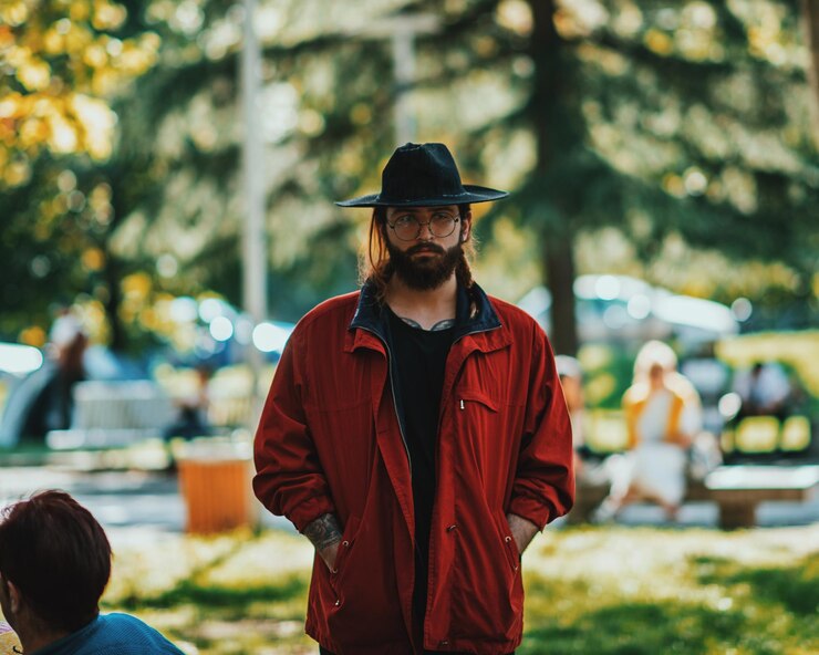 Foto retrato de un joven con las manos en los bolsillos usando un sombrero mientras está de pie en el parque
