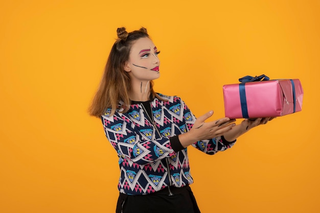 Retrato de una joven con maquillaje creativo y sosteniendo una caja de regalo envuelta con fondo naranja. foto de alta calidad