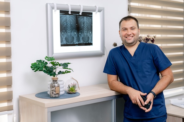 Retrato de joven médico en matorrales de pie junto a la placa de luz con resultados de resonancia magnética. Retrato de médico de sexo masculino en la sala médica moderna.