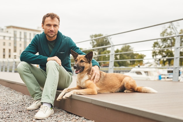 Retrato de joven mirando a la cámara mientras está sentado con su perro en la calle al aire libre