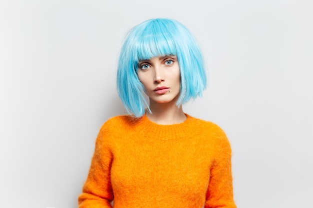 Retrato de joven moda con cabello azul en suéter naranja contra la pared blanca.