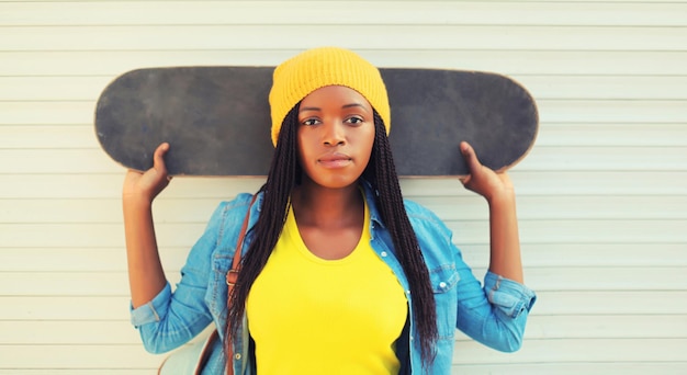 Foto retrato de una joven modelo africana moderna posando con ropa de colores con patineta en la ciudad