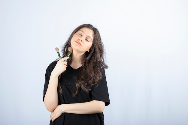 Retrato de joven modelo aplicar maquillaje con pincel en blanco.