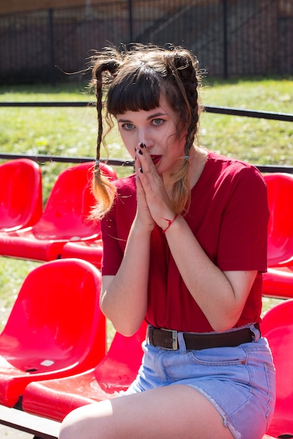 Retrato de joven modelo de chica tennager hermosa normal en los asientos de un estadio de béisbol vistiendo camiseta roja