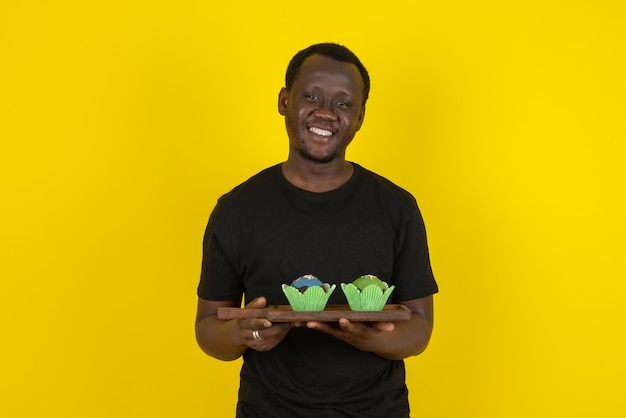 Retrato de un joven modelo sosteniendo deliciosos cupcakes contra la pared amarilla