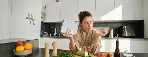 Retrato de una joven moderna cocinando haciendo lista de compras leyendo recetas y haciendo ensalada de comida