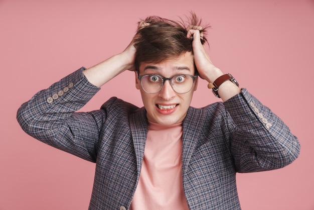 Retrato de un joven molesto con chaqueta que se encuentran aisladas en rosa, tirando de su cabello