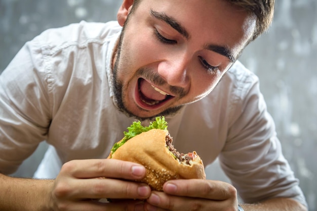 Retrato de un joven mordiendo una hamburguesa con la boca abierta