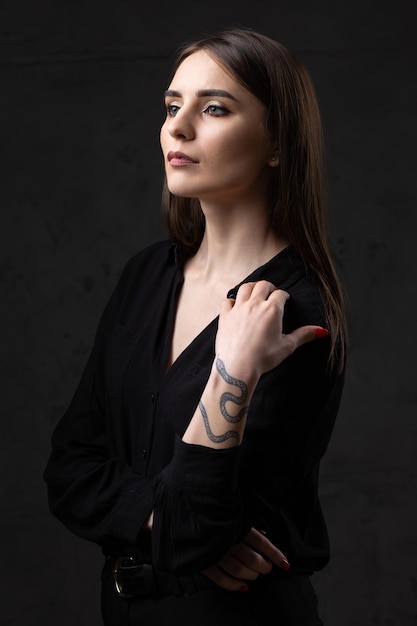 Retrato de una joven morena con cabello largo en el estudio Foto dramática en colores oscuros Una niña con un tatuaje de serpiente en el brazo