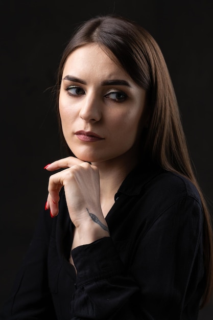 Retrato de una joven morena con cabello largo en el estudio Foto dramática en colores oscuros Una niña con un tatuaje de serpiente en el brazo