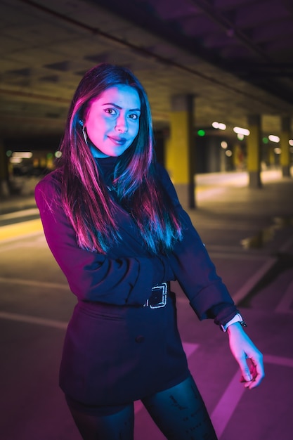 Retrato de joven morena caucásica por la noche en un estacionamiento subterráneo, iluminado con neón