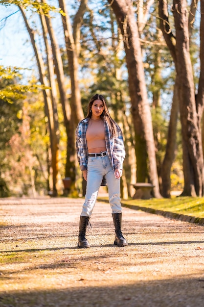 Retrato de una joven morena caucásica con un suéter de lana a cuadros y jeans rotos en un parque