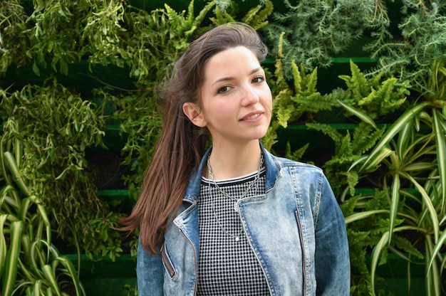 Retrato de una joven morena en una chaqueta de mezclilla. contra el espacio de las plantas verdes