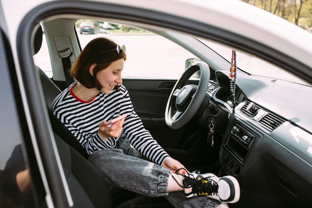 Retrato de una joven morena conduciendo en un coche usando un teléfono inteligente