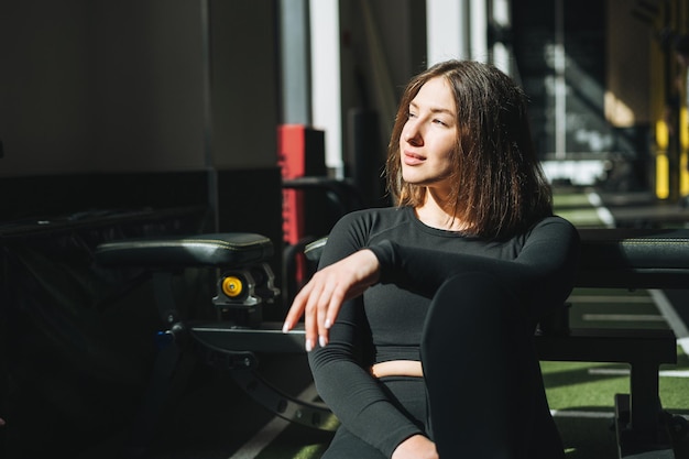 Retrato de una joven morena descansando con ropa deportiva activa en el gimnasio