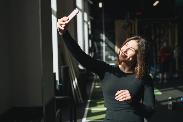 Foto retrato de una joven morena descansando en ropa deportiva activa tomando una selfie en un club de fitness