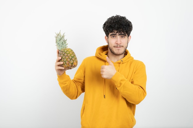 Retrato de un joven morena mostrando el pulgar hacia arriba y sosteniendo la piña.