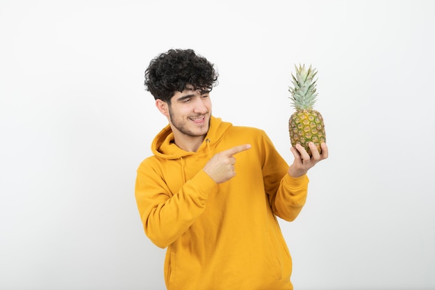 Retrato de un joven morena de pie y apuntando a la piña.