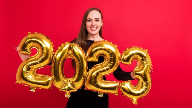 Retrato de una joven morena sosteniendo los números del año nuevo 2023 en un fondo rojo