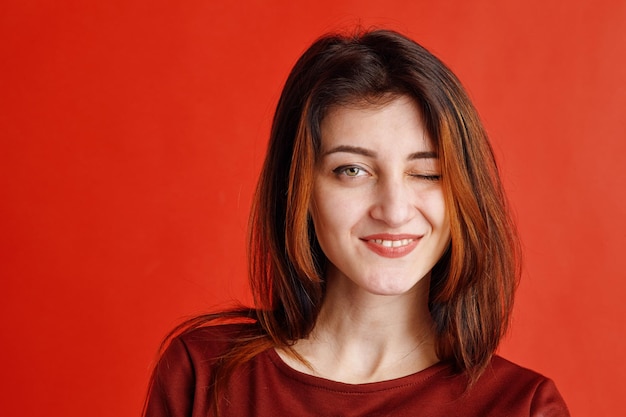 Retrato de una joven morena vestida con blusa roja dando un guiño