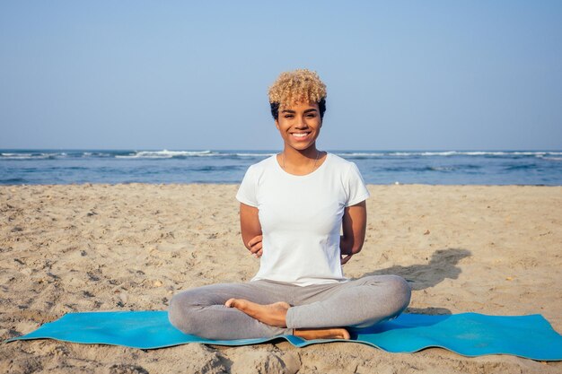 Retrato de una joven mujer africana latina sentada en una pose de yoga en el estilo de vida de la playa