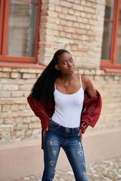 Retrato de una joven mujer afroamericana caminando por la calle vestida con jeans y una chaqueta roja