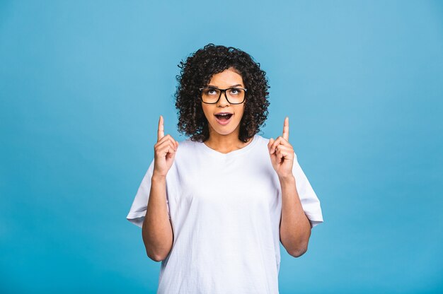 Retrato de una joven mujer afroamericana feliz apuntando con el dedo en el espacio de la copia aislado sobre fondo azul.