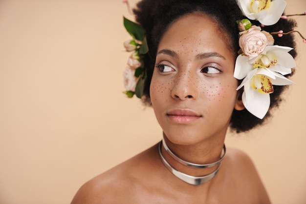 Retrato de joven mujer afroamericana pecosa semidesnuda con flores en el pelo