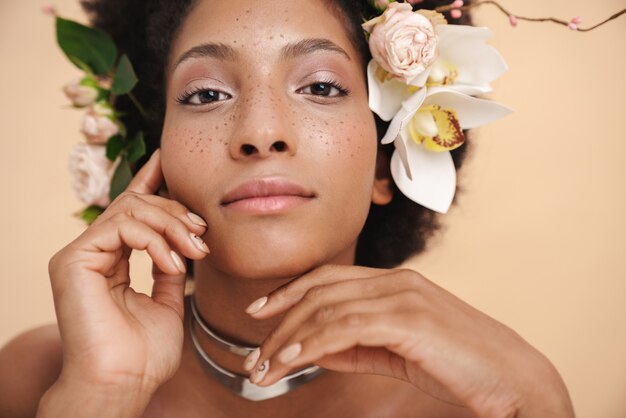 Retrato de joven mujer afroamericana pecosa semidesnuda con flores en el pelo