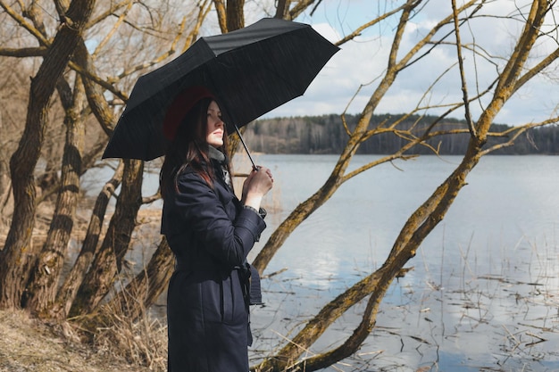 Retrato de una joven mujer agradable con paraguas negro al aire libre