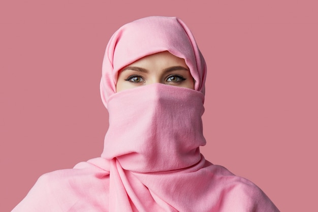 Retrato de joven mujer árabe musulmana vistiendo coloridos hijab contra pared rosa