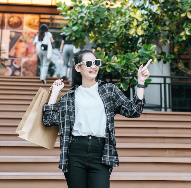 Retrato de joven mujer asiática con anteojos bajando escaleras con bolsa de papel de compras