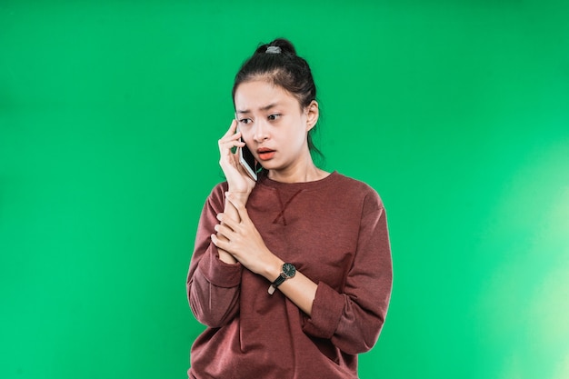 Retrato joven mujer asiática hablando por teléfono con una expresión triste y conmocionada sobre un fondo verde