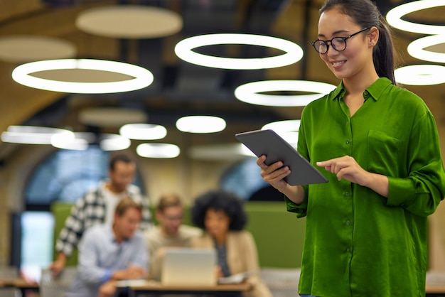 Foto retrato de joven mujer asiática inteligente con tableta digital mientras está de pie en el espacio de coworking