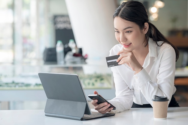 Retrato de joven mujer asiática con smartphone y tarjeta de crédito mientras está sentado en el escritorio de oficina.