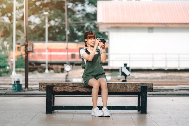 Retrato Joven mujer asiática sonriente turista Chica viajera caminando y sosteniendo la cámara espera el viaje en tren se toma en la plataforma ferroviaria Tailandia verano relax vacaciones Concepto