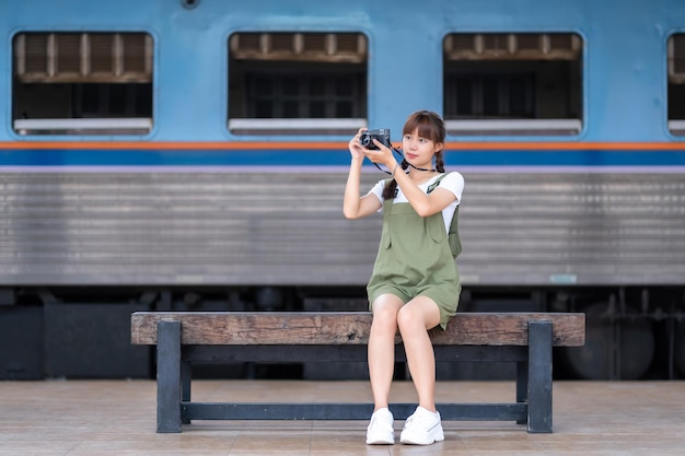 Retrato Joven mujer asiática sonriente turista Chica viajera caminando y sosteniendo la cámara espera el viaje en tren se toma en la plataforma ferroviaria Tailandia verano relax vacaciones Concepto