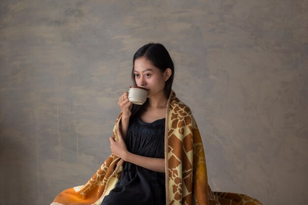 Retrato de joven mujer asiática tomando café y relajándose en el sofá