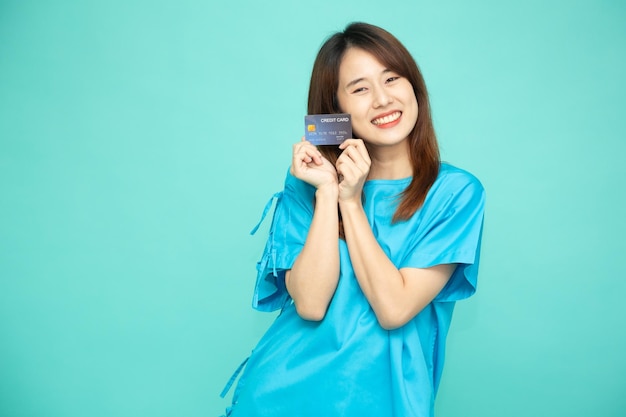 Retrato de joven mujer asiática en traje azul paciente sosteniendo tarjeta de crédito aislado sobre fondo verde