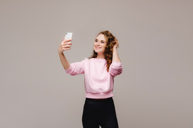 Retrato de una joven mujer atractiva haciendo foto selfie en smartphone aislado sobre un fondo blanco.