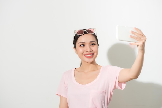 Retrato de una joven mujer atractiva haciendo foto selfie en smartphone aislado sobre un fondo blanco.