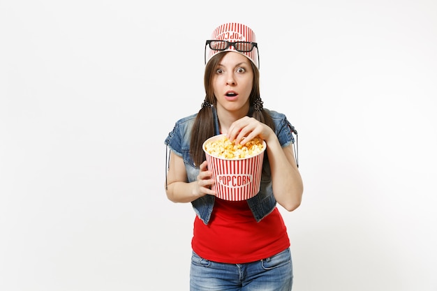 Retrato de joven mujer atractiva sorprendida en gafas 3d con cubo de palomitas de maíz en la cabeza viendo películas, comiendo palomitas de maíz de cubo aislado sobre fondo blanco. Emociones en el concepto de cine.