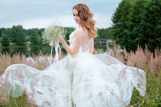 Retrato de joven mujer bonita (novia) en vestido de novia blanco al aire libre, peinado