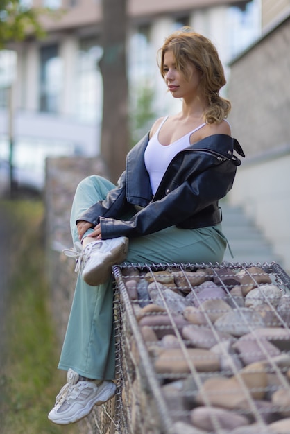 Retrato de una joven mujer bonita en pantalones cortos azul sentado en un banco en el patio de un complejo residencial.