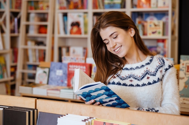 Retrato de una joven mujer bonita de pie y leyendo un libro en la biblioteca